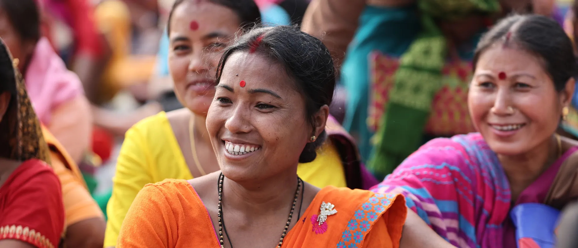 A smiling woman among a diverse gathering of community members.