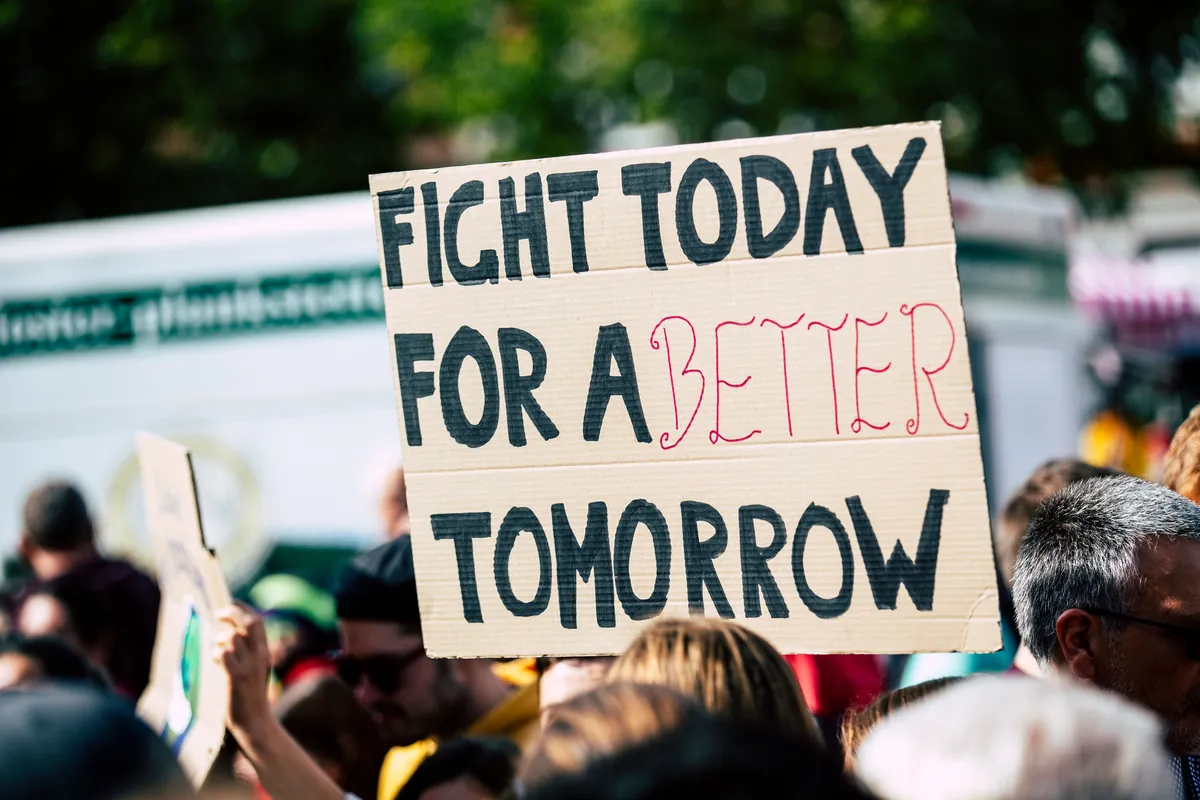 A protester holds a cardboard sign reading 'Fight today for a better tomorrow.'